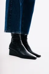 Bota de caña media en cuero negro, con diseño de punta cuadrada y taco cuña integrado.