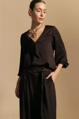 Blusa de satén color marrón oscuro, con escote en V y detalle de volado frontal. Presenta mangas tres cuartos con terminación holgada y una caída fluida y elegante.