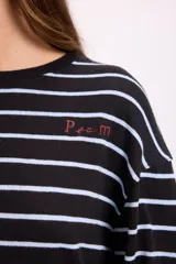 Remera de manga larga con diseño oversize, confeccionada en tejido de punto grueso a rayas horizontales en tonos marrón y blanco. Presenta cuello redondo y un pequeño bordado distintivo en el pecho.