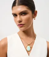 Conjunto de joyería compuesto por un collar largo con cadena tipo cola de ratón y un dije ovalado con piedra central verde agua y marco de metal martillado, acompañado por un par de aros tipo argolla pequeña.