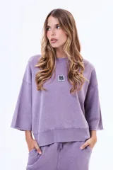 Buzo de felpa con cuello redondo, mangas tres cuartos con terminación desflecada y corte holgado. Presenta un aplique metálico cuadrado en el centro del pecho con la inscripción 'Self Love Club'.