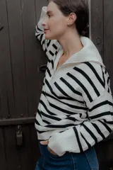 Buzo de punto con diseño a rayas horizontales en blanco y negro. Presenta cuello alto con cierre frontal parcial y mangas largas con puños acanalados.