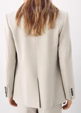 Blazer color beige con solapas de muesca, cierre frontal de dos botones oscuros, bolsillos con solapa en los laterales y un bolsillo ojal en el pecho.