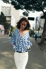 Camisa de rayas verticales azules y celestes, con cuello solapa, escote en V, cierre frontal con botones y mangas largas abullonadas con puños ajustados.
