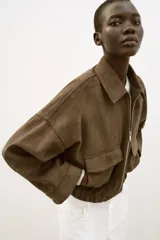 Cazadora de efecto ante con cuello solapa, cierre frontal con cremallera y mangas por debajo del codo. Presenta bolsillos delanteros de plastrón con solapa y bajo elástico.