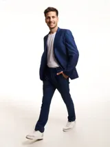 Traje de dos piezas compuesto por un saco de corte slim con solapas clásicas y bolsillos frontales, y un pantalón de corte ajustado. El conjunto presenta un diseño liso en color azul.