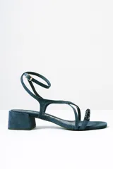 Sandalias de taco cuadrado medio, confeccionadas en gamuza color azul. Presentan tiras finas que cruzan el empeine, una pulsera ajustable al tobillo y detalle de cuentas decorativas en la tira frontal.