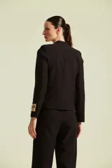 Saco negro de inspiración militar de la marca Natalia Antolin, con intrincados bordados dorados en el frente y detalle de etiqueta de la marca en la manga izquierda.