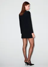 Vestido tipo blazer de corte corto y color negro, con solapas de muesca, doble botonadura frontal y bolsillos de ojal con solapa.