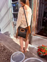 Cartera bandolera negra de cuero con forro interno de tela, detalle de flecos de cuero marrón en la parte inferior y asa larga regulable.