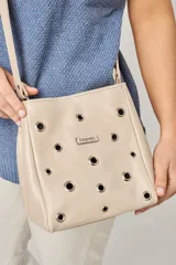 Bandolera de cuero color beige con diseño de ojales metálicos distribuidos por toda la superficie frontal y placa metálica con logo de la marca. Cuenta con correa larga ajustable.