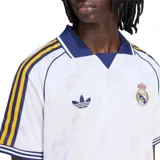Camiseta de fútbol Adidas Originals del Real Madrid, color blanco con cuello polo y detalles en azul y amarillo en las mangas y hombros.