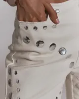 Jeans de corte recto color crudo con apliques de tachas metálicas plateadas distribuidas en patrones geométricos.