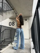Jeans rígido de corte wide leg, tiro medio y color celeste, con diseño de estrellas grandes desflecadas en los laterales de las piernas.