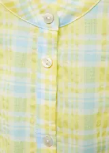 Vestido camisero corto con estampado de cuadros amarillos y celestes. Tiene cuello mao, mangas largas con puños abotonados y cierre frontal con botones. Incluye lazo decorativo en la cintura.