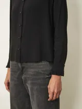 Camisa de manga larga color blanco, con cuello alto tipo mao con detalle de volados y cierre frontal de botones.