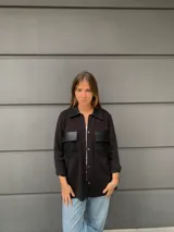 Camisa negra de tejido de punto con cuello clásico, cierre frontal con botones y dos bolsillos de cuero en el pecho.