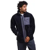 Canguro de sherpa con cierre frontal completo, cuello alto y bolsillo en el pecho con cierre. Presenta una combinación de texturas en color negro y gris oscuro, con diseño funcional y térmico.
