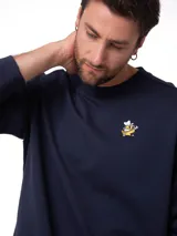 Buzo de felpa azul marino con cuello redondo, gráfico bordado en el pecho izquierdo y etiqueta con el logo Cat en el puño de la manga izquierda.