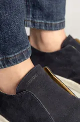 Botineta masculina de gamuza en color azul marino, con diseño slip-on sin cordones y suela de goma blanca. Presenta costuras visibles en la puntera y un estilo urbano minimalista.