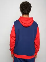 Canguro de felpa Umbro del Club Nacional de Football, con diseño tricolor en rojo, azul y blanco. Presenta capucha con cordones ajustables, bolsillo tipo canguro frontal, logo de la marca y escudo del club bordados en el pecho.