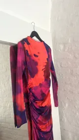 Vestido midi ajustado con estampado abstracto en tonos naranja, rosa y azul. Tiene cuello alto y mangas largas.