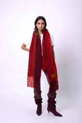 Bufanda de lana merino tejida en telar, con diseño de rayas en tonos marrón, beige y rojo. Presenta flecos en los extremos y un parche negro con la palabra "CAPER" en blanco.