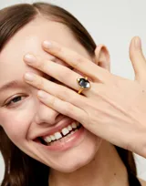 Anillo dorado con un cristal facetado gris en forma de lágrima.