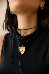 Collar con dije de corazón en acero quirúrgico, con textura irregular y relieve, montado sobre un tiento encerado negro.