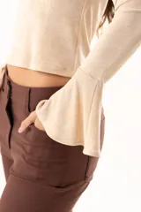 Blusa beige con hombros descubiertos, confeccionada en tela elástica con destellos de lurex. Presenta mangas largas con terminación acampanada y diseño ajustado al cuerpo.