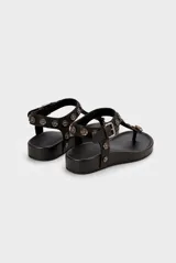 Sandalia baja de cuero vacuno color negro, tipo thong sandal, con tira vertical en el empeine decorada con apliques metálicos en forma de flores y tira ajustable en el talón con hebilla.