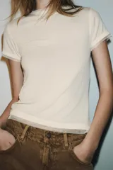 Camiseta de manga corta color marrón oscuro con textura acanalada, cuello redondo y bajo recto. Presenta un bajo superpuesto de tul o tela más clara, visible en el ruedo y en el cuello.