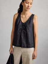 Top sin mangas de lino color negro con escote en V y detalle de bordado central en forma de trébol de cuatro hojas. Presenta costuras decorativas visibles en el escote y el ruedo.