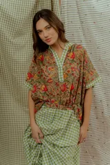 Blusa de algodón con estampado floral multicolor, con detalles en tela a cuadros verde y blanca en el cuello en V, la pechera y los bordes de las mangas cortas.