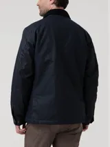 Chaqueta de hombre color azul marino, confeccionada en tela encerada impermeable y cortaviento. Cuenta con cuello de cotelé, cierre frontal con broches y cremallera, y múltiples bolsillos exteriores e interiores. El interior está forrado en franela y tiene relleno de THERMORE, hecho de fibras recicladas.