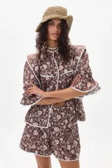 Camisa marrón con estampado floral, cuello con volados y mangas 3/4 con puños elásticos.