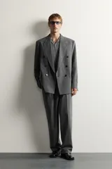Blazer gris de corte relaxed fit con diseño de raya diplomática, cuello con solapas de pico, doble botonadura cruzada y bolsillos con solapa en la cadera.