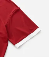 Remera de manga corta estilo polo, color rojo, con cuello y puños en contraste blanco. Presenta un corte oversized con hombros caídos y la palabra "ATHLÈTES" estampada en blanco en el frente. Incluye pequeños gráficos blancos a cada lado del pecho.