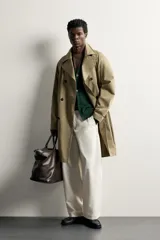 Trench regular fit de color beige, confeccionado en tejido técnico repelente al agua, con diseño de botonadura cruzada, cuello con solapas, mangas raglán con trabillas ajustables en los puños y cinturón del mismo tejido.