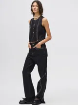 Pantalón de denim tiro alto con corte oxford y aberturas laterales en el bajo. Presenta apliques metalizados decorativos en los bolsillos delanteros y a lo largo de las costuras laterales.