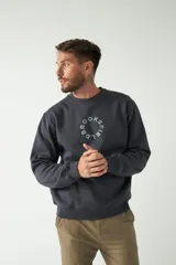 Buzo de felpa color beige con cuello redondo, manga larga y puños acanalados. Presenta un logo circular estampado en el frente.