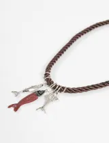 Collar con cordón trenzado de color marrón oscuro, adornado con tres dijes colgantes con forma de pez: uno plateado liso, uno plateado con textura y esmalte rojo, y uno plateado liso.