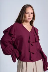 Blusa de manga larga color bordó con escote en V, detalle de volados en los hombros y el frente, y puños elásticos con terminación acampanada.