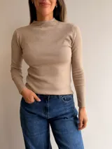 Media polera de tejido fino color gris, con cuello alto, manga larga y corte ajustado al cuerpo.