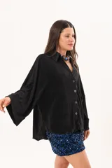 Camisa negra plisada de manga larga con puños vueltos, cuello camisero y cierre frontal de botones claros.