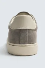 Zapatilla deportiva de hombre confeccionada en piel con acabado de serraje. Presenta un diseño minimalista con cordones al tono y un detalle en contraste de color en la pieza del talón. Cuenta con una suela de goma con volumen.