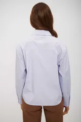 Camisa de vestir holgada, color celeste claro, con finas rayas verticales blancas y detalles de lentejuelas blancas dispersas por toda la prenda. Posee cuello camisero y cierre frontal de botones.