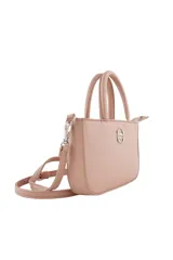 Cartera tipo bandolera de diseño compacto, color rosado, con doble asa superior y correa ajustable extraíble. Presenta un aplique metálico circular con logo en el centro y cierre superior.