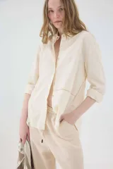 Camisa de lino blanca, de silueta oversize y calce relajado, con mangas largas y detalles de puntillas en la delantera.
