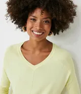 Blusa de punto color amarillo claro, con escote en V, mangas largas con textura acanalada y diseño de ruedo asimétrico tipo mullet con aberturas laterales.